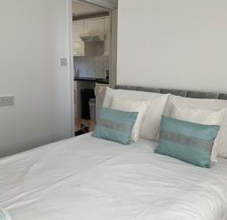 A bedroom with a bed and pillows visible towards a kitchen at Bungalow Sleeps 2 Parking in Newquay
