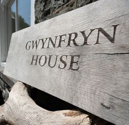 A wooden sign displaying Gwynfryn House outside a stone wall in Llanbedr