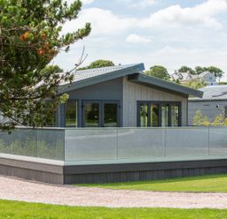 A house with a deck and glass railing at Hideaway Lodge Llanfechell