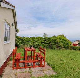 A table and benches with grass and bushes at Cottage 28 in Brixham