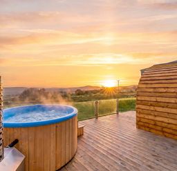 A hot tub on a wooden deck during sunset at The Lodge at Brambles Farm Sleeps 4 Hot Tub Leek