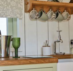 A kitchen with mugs on a shelf and glassware on the countertop at Cosy Luxury Owls Roost Hut with Private Hot Tub near Little Deptford Farm