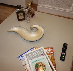 A coffee table with a bowl, magazines, a bottle of liqueur, and a remote control at Cornerhouse Apartment 3 Llandudno