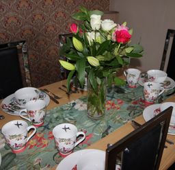 A dining table set with plates and cups along with flowers at Cornerhouse Apartment 5 Llandudno