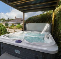 A hot tub under a canopy with a house in the background at Honey Bee Cottage Menheniot