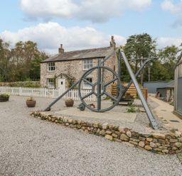 An outdoor area with a stone house and mechanical wheel at Irt Cottage in Seascale