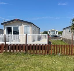 A static caravan with a deck and fenced area at Unity Beach in Burnham-on-Sea