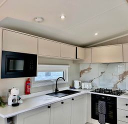 A kitchen with a sink, gas stove, microwave, and kettle at Lovely Holiday Home On Waxham Sands, Great Yarmouth