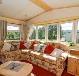 A living room with a floral sofa and large windows at Leven in Lampeter