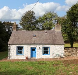 A cottage with blue windows and door surrounded by trees at Felin Bach Aberdaron