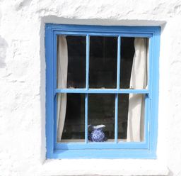 A window with blue frame and curtains at Felin Bach in Aberdaron