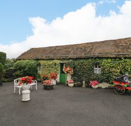 A garden area with a thatched roof building and flower pots at Teresa's Cottage