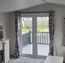 A living room with a television and door leading to a deck at 3 Bedroom Cabin Sleeps 6 - Shared Pool & Shared Hot Tub, Flamingo Land Resort near Malton