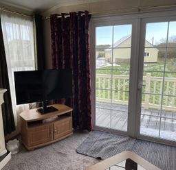 A living room with a television and door leading to the deck at Chalet Sleeps 4 Near Cymyran Beach Caergeiliog