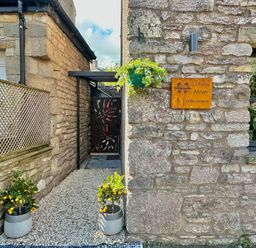 An entrance with stone walls and potted plants at Muddy Boots – La Petite Mews in Kirby Stephen