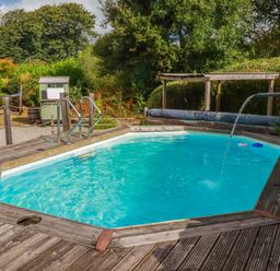 A swimming pool with handrails and decking in the garden at Honey Bee Bus Menheniot