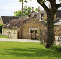 A cottage with a fence and a tree in the garden at Peewit Barn in Moreton-in-Marsh