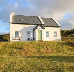 A house with green door and windows set in a garden at Doughbeg Beach Cottage in 