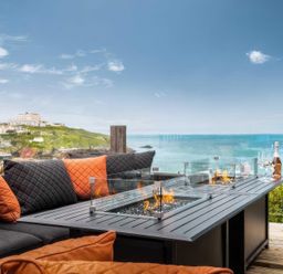 An outdoor seating area with fire table and cushions at By The Sea in Newquay