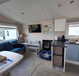 A living room with a blue sofa and television at Lyons Sunnysands - Snowdon Summit 050 in Talybont