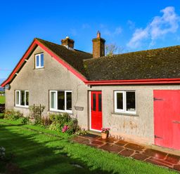 A house with a red door and windows surrounded by grass and flowers at The Bungalow in Penrith