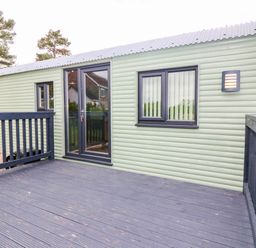 An outdoor view of a cabin with a deck and multiple windows at Calendonia Hut West Mains near Haggerston