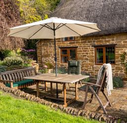 A patio with a table and umbrella near a stone house at a cottage property