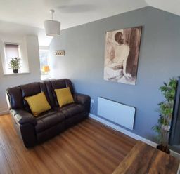 A living room with a sofa, lamp, plant, and artwork at 1 Bedroom Apartment with Sea View, Mevagissey