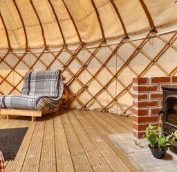 A seating area with armchairs and a wood stove at Yurt, Sleeps 2 with BBQ and Fire Pit, Tregooden Farm near St Tudy