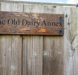 A wooden sign on a fence stating The Old Dairy Annex