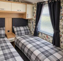 A bedroom with two single beds and curtains at 3 Bedroom Seafront Caravan, Sleeps 6 with Parking