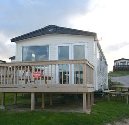 A mobile home with a deck and sign at Perran Sands Holiday Park - 615 Chy-an-Mor Perranporth