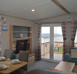 A living room with a television and balcony view at Perran Sands Holiday Park - 615 Chy-an-Mor Perranporth