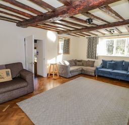 A living room with brown and blue sofas wooden beams on the ceiling and a large window at Little Cowarne Court Little Cowarne near Bromyard