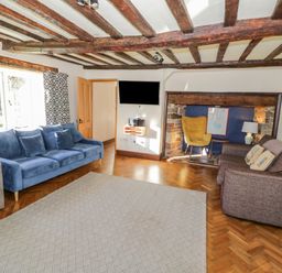A living room with wooden ceiling beams blue and brown sofas a yellow chair and a wall-mounted television at Little Cowarne Court in Little Cowarne near Bromyard