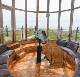 A room with curved seating and a mounted viewing device surrounded by large windows at Old Higher Lighthouse Stopes Cottage Portland Bill