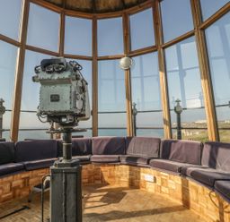An observation room with large windows a mounted binocular viewer and a circular bench with cushions at Old Higher Lighthouse Branscombe Lodge Portland Bill
