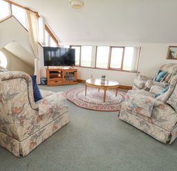 A living room with floral armchairs a round coffee table a television on a wooden stand and windows at Old Higher Lighthouse Branscombe Lodge Portland Bill