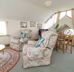 A sitting area with two floral armchairs a round wooden table and a dining table with chairs near windows at Old Higher Lighthouse Branscombe Lodge Portland Bill