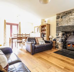A living room with two leather sofas a wood-burning stove dining table and chairs a wooden bookshelf and wooden flooring at 3 Railway Cottages in Betws-y-Coed
