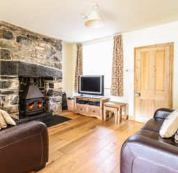 A living room with a stone fireplace two leather sofas a wooden floor and a television at 3 Railway Cottages Betws-y-Coed