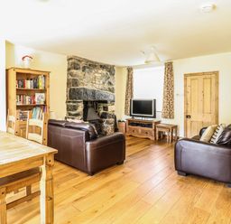A living room with a stone fireplace brown leather sofas wooden dining table bookshelf television and carpeted stairs at 3 Railway Cottages in Betws-y-Coed