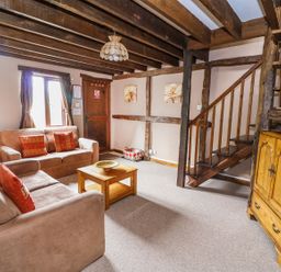 A living room with two beige sofas and a wooden coffee table next to a staircase at Cedar Cottage in Llanidloes