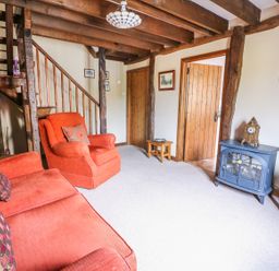 A living room with wooden beams orange sofa and armchair and a blue stove at Beech Cottage in Llanidloes