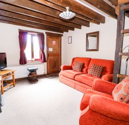 A living room with red sofa and armchair TV and wooden beams on ceiling at Beech Cottage in Llanidloes