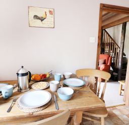 A dining table set with plates bowls mugs and fruit bowl with a roosting chicken picture on the wall at Beech Cottage in Llanidloes