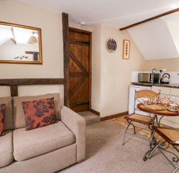 A small room with a beige sofa with two cushions a wooden door a mirror a table set with tea cups and a teapot next to a compact kitchen area at Oak Cottage in Llanidloes