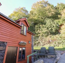 Exterior of a wooden house with a flower box and two chairs near a gravel path at Oak Cottage in Llanidloes