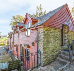 A row of houses with red wooden siding and stone walls on a hillside with outdoor seating at Oak Cottage in Llanidloes