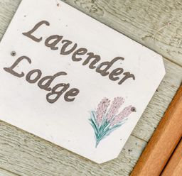 A wooden sign with the text Lavender Lodge and a small painting of lavender flowers on a textured wooden wall at Lavender Lodge in Charlton Horethorne near Sherborne